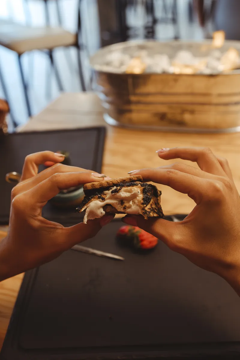 Manos partiendo un s’more recién asado en una mesa de D’Fogata